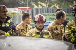 zdjęcie przedstawia policjantów i strażaków stojących przy wraku samochodu i omawiających ćwiczenie