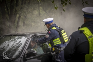 zdjęcie przedstawia wrak z unoszącym się dymem spod maski i policjantów udzielających pomocy