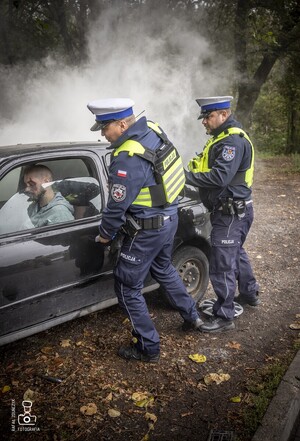 zdjęcie przedstawia wrak z unoszącym się dymem spod maski i policjantów udzielających pomocy