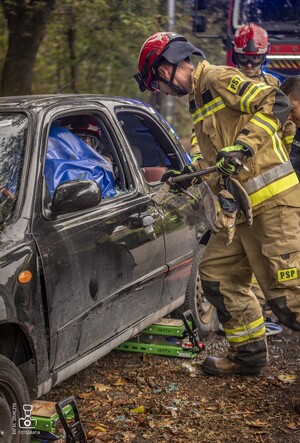 zdjęcie przedstawia wrak samochodu i strażaków rozcinających drzwi