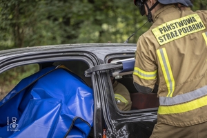 zdjęcie przedstawia wrak samochodu i strażaków rozcinających drzwi